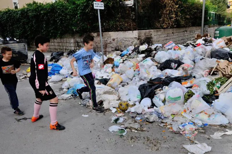Bambini giocano a pallone vicino ad una montagna di rifiuti a Palermo