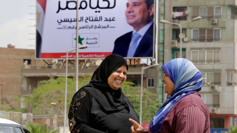 Due donne parlano per la strada. Sullo sfondo un manifesto elettorale inneggia a Sisi