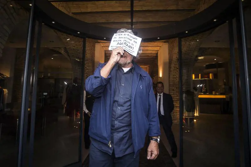Beppe Grillo lascia l'hotel a Roma. Sul volto un foglio in cui chiede di sostenere una Onlus