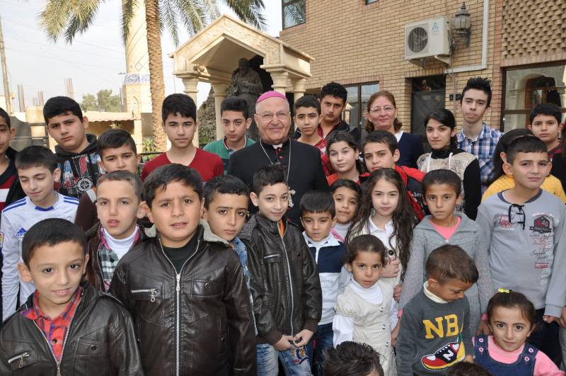 Monsignor Shlemon Warduni con i bambini del catechismo nella parrocchia del Sacro cuore di Baghdad con la statua di padre Pio sullo sfondo