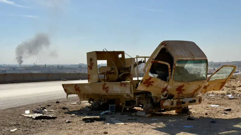 Carcassa di un mezzo dell'esercito di Assad alle porte di Damasco e colonna di fumo di bombardamento israeliano o arsenale che brucia