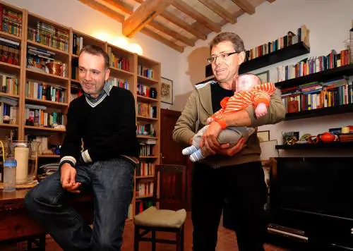 Il piccolo David in braccio a Valter e Mario, la coppia gay livornese che lo ha avuto da una donna che ha dato l'utero in affitto