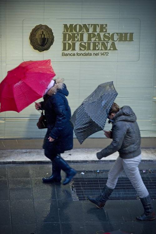 Passanti si riparano dalla pioggia nei pressi di una filiale di Mps