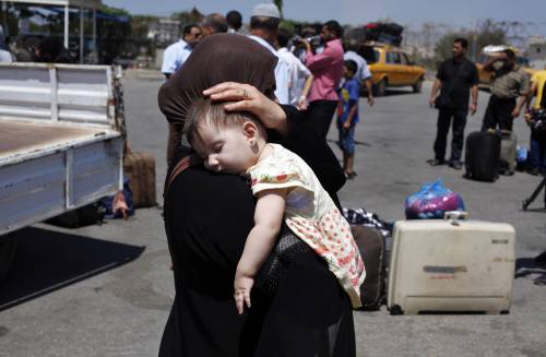 Una donna si allontana dal valico di Rafah con un bambino in braccio