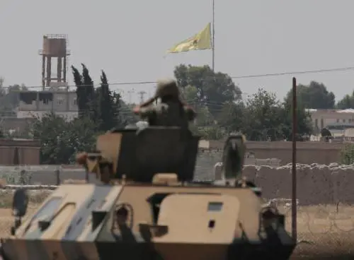 Un soldato turco scruta la bandiera del Ypg che sventola a Tal Abyad