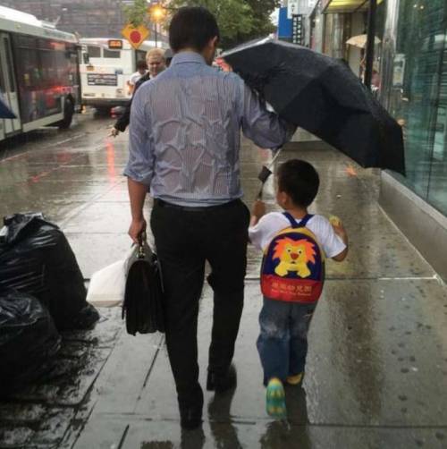 Il papà che protegge il figlio dalla pioggia