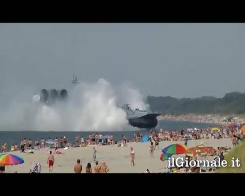 Nave militare attracca sulla spiaggia affollata