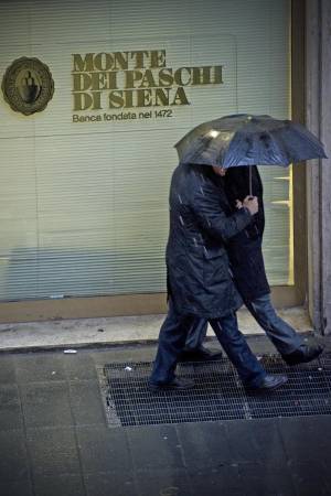 Alcune persone si riparano dalla pioggia nei pressi di una filiale della banca Monte Paschi di Siena