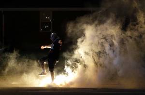 Un manifestante allonta un lacrimogeno lanciato dalla polizia