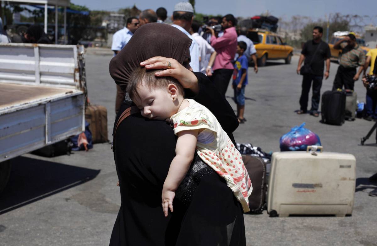 Una donna si allontana dal valico di Rafah con un bambino in braccio