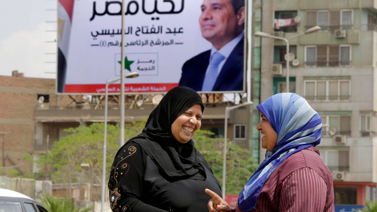 Due donne parlano per la strada. Sullo sfondo un manifesto elettorale inneggia a Sisi
