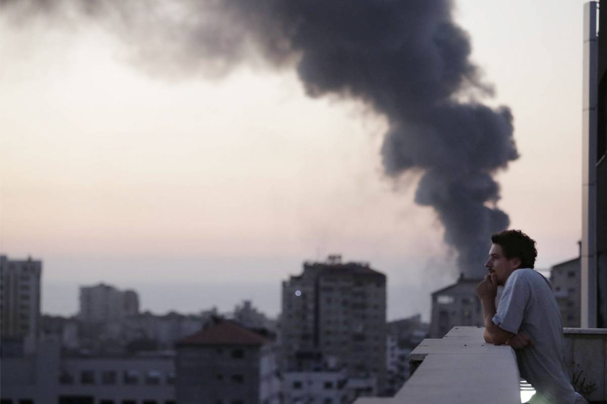 Il videoreporter italiano Simone Camilli. Sullo sfondo, fumo sale dopo un attacco israeliano