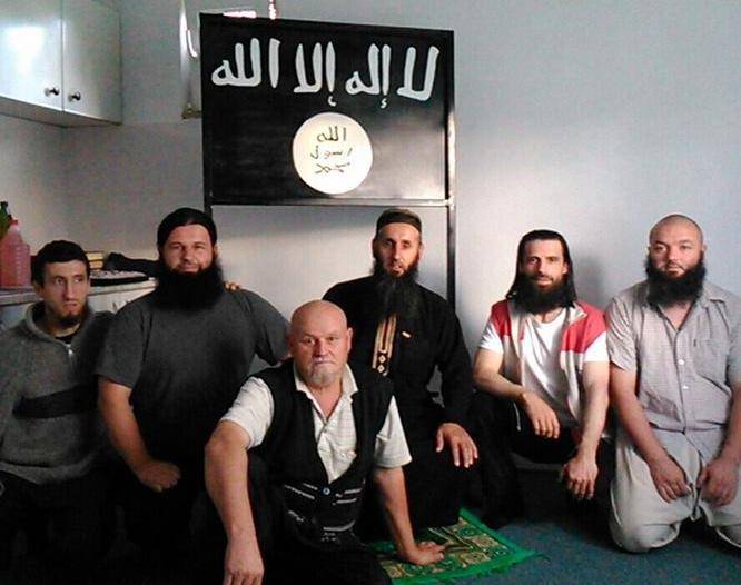 L'imam Bilal Bosnic (vestito di nero e con la barba più lunga) in mezzo ai suoi seguaci. Alle spalle la bandiera del Califfato