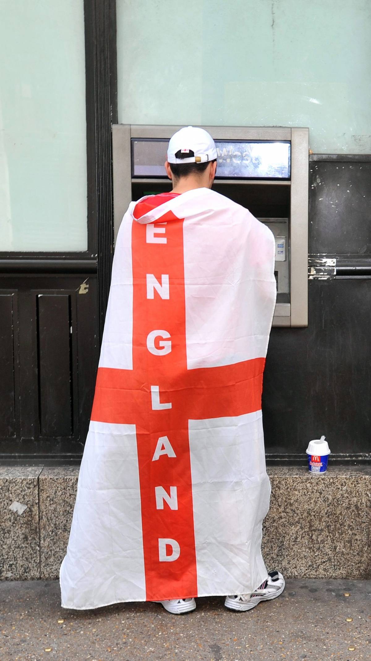 Un fan della nazionale di calcio inglese al bancomat, con la bandiera sulle spalle
